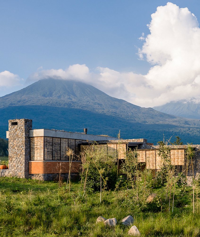 Singita Kwitonda Lodge, a low stone and timber building below a Virunga volcano