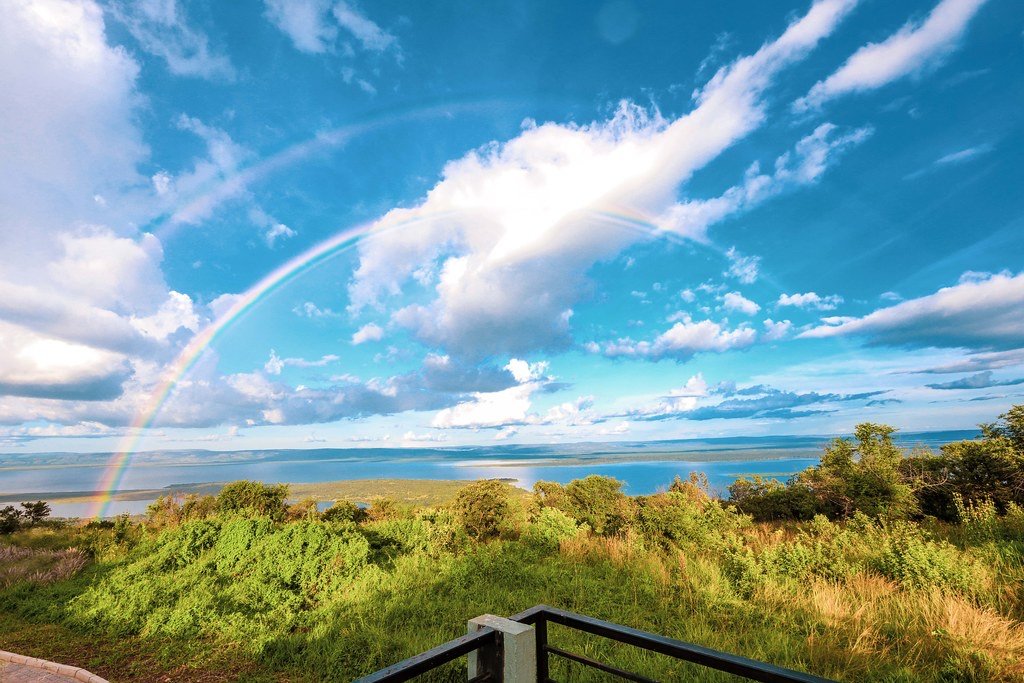 A rainbow arching over a lake and green hills seen from a viewpoint in Akagera National Park, Rwanda
