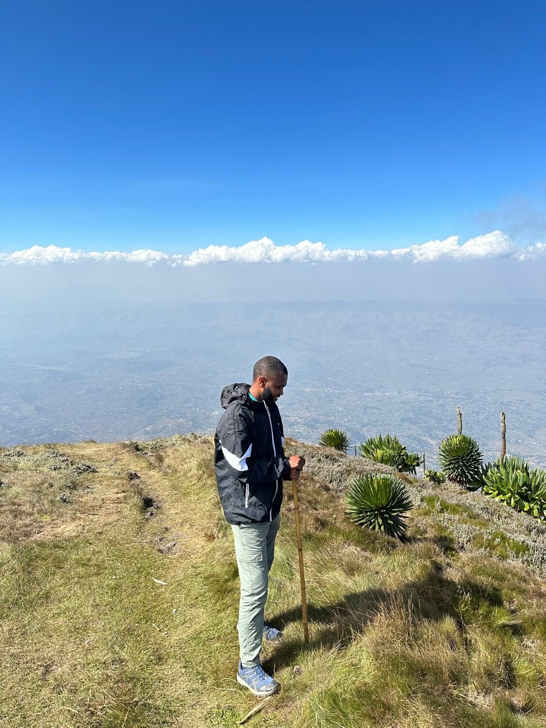A hiker on the summit ridge of Mount Muhabura above a layer of cloud