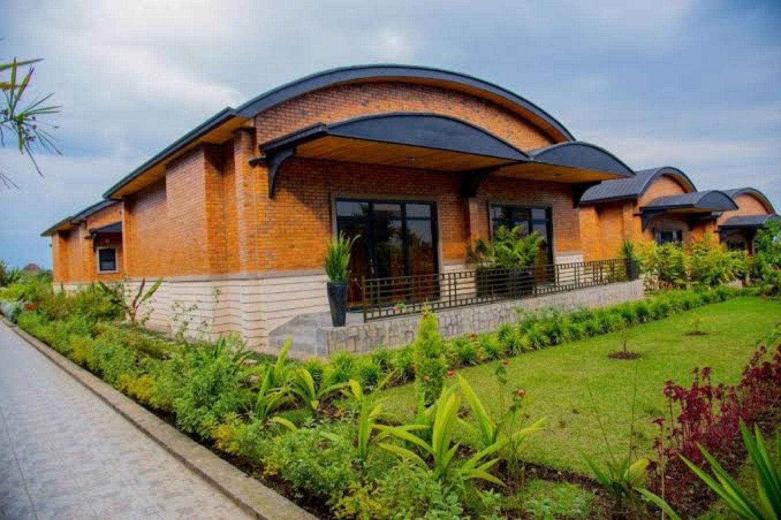 Brick building with curved roofs and a garden path at Virunga Inn Resort & Spa, Kinigi